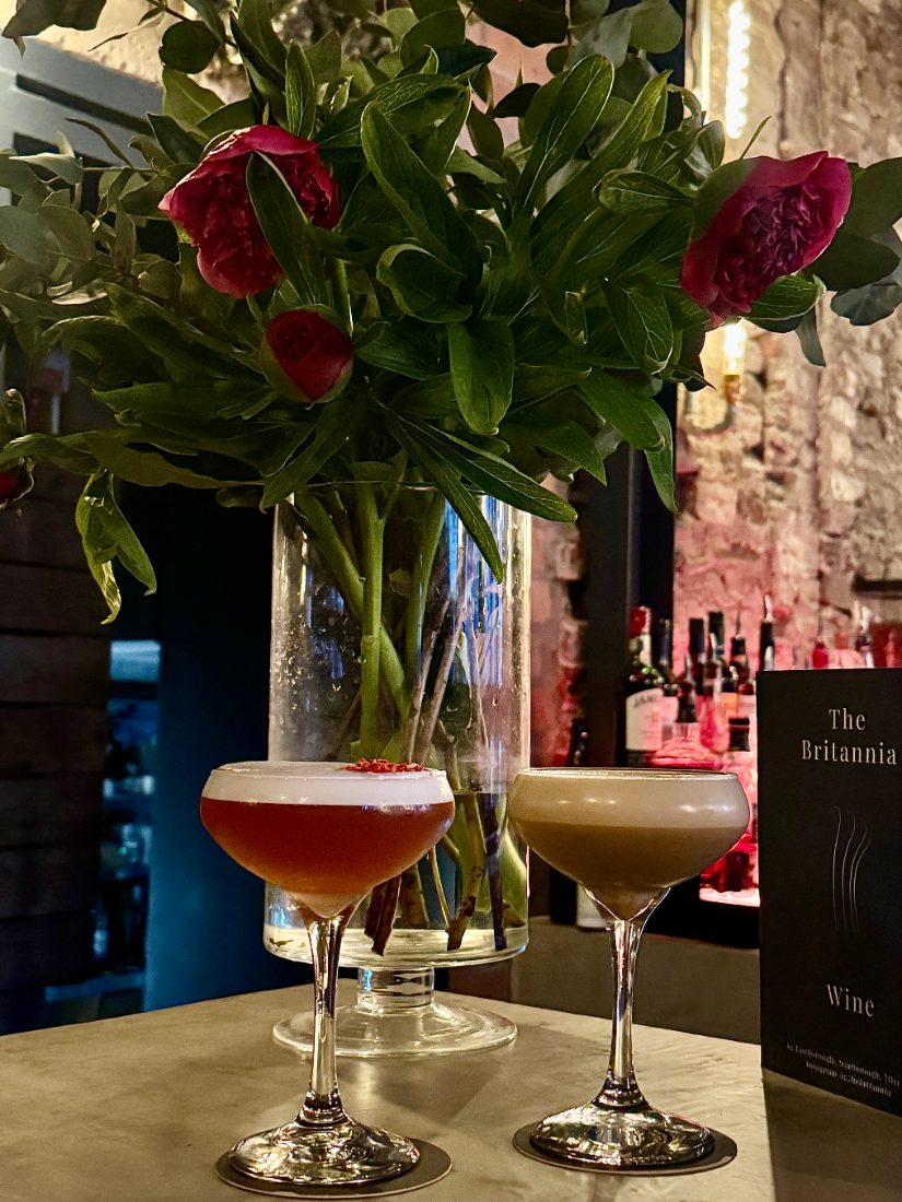 Two cocktails on the bar beside peonies